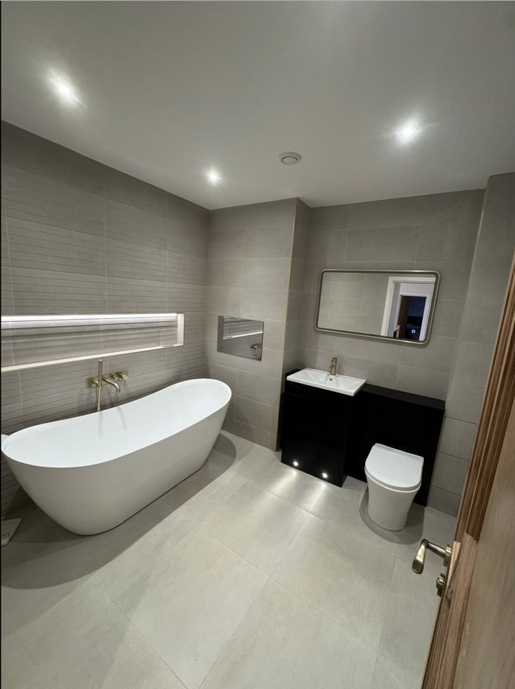 A finished bathroom with a freestanding bath, lit tiled niche and brushed gold taps