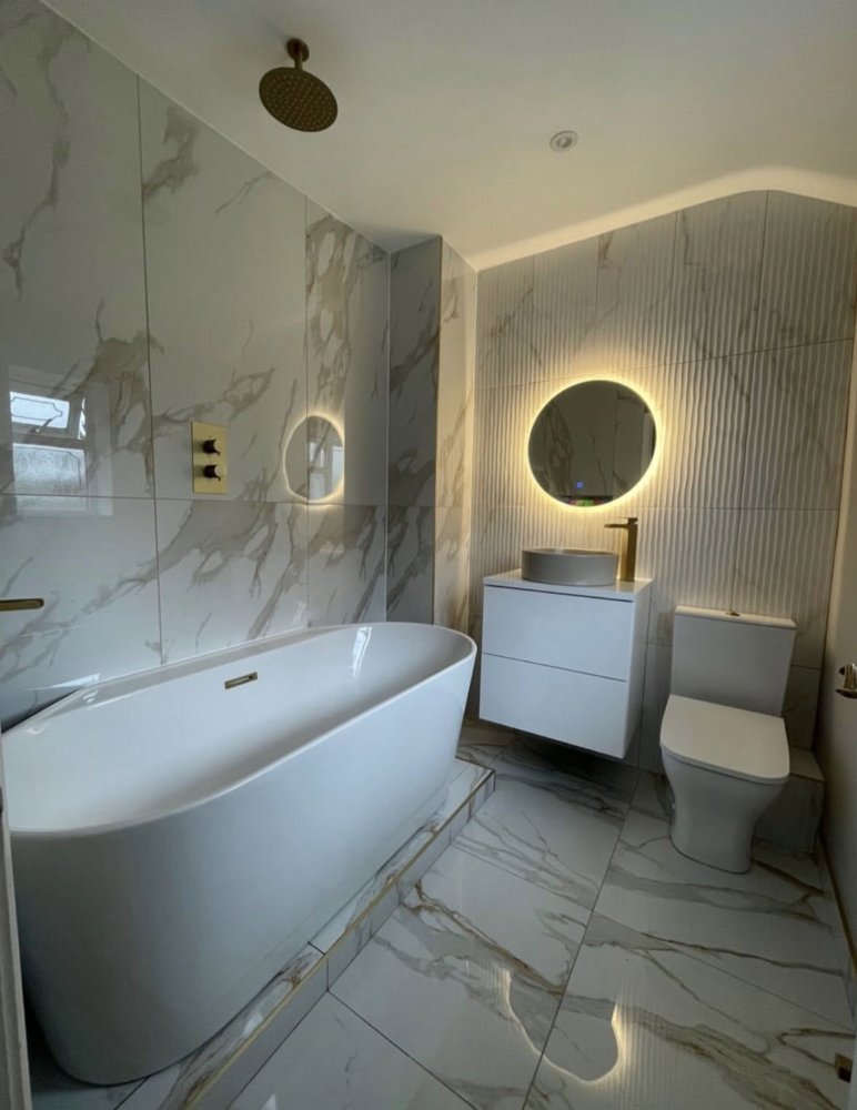 A finished bathroom with marble-effect tiles, freestanding bath and brushed gold fittings