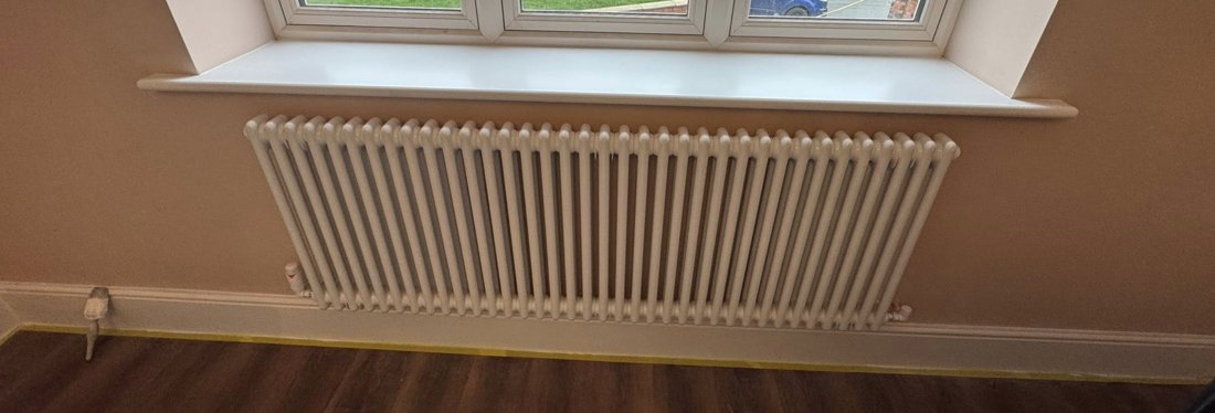 A white column radiator fitted under a living room window