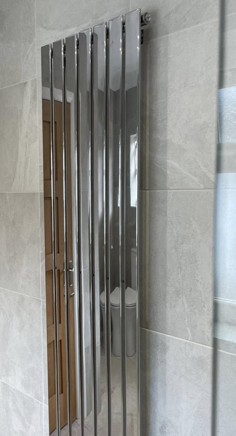 A tall chrome designer radiator in a tiled bathroom